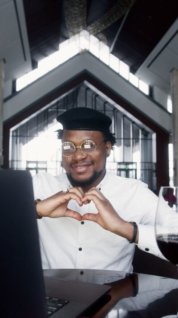 Stylish man with glasses makes heart gesture in modern indoor setting.